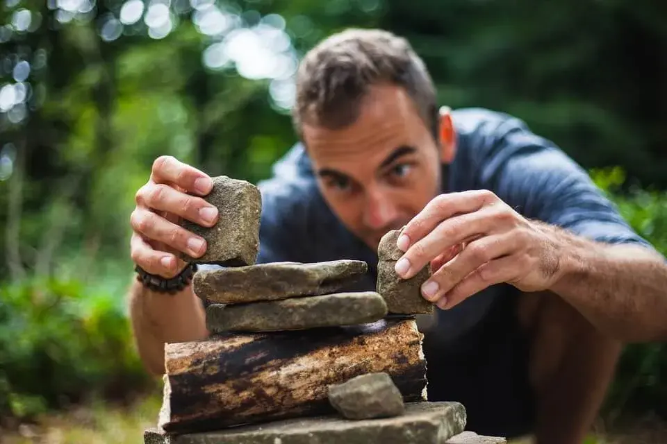 На фото мужчина строит фигуру из камней